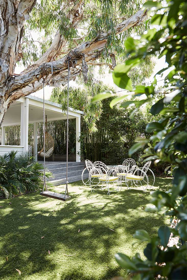 Lush front yard with vintage outdoor setting and tree swing at The Cottage, Byron Beach Abodes