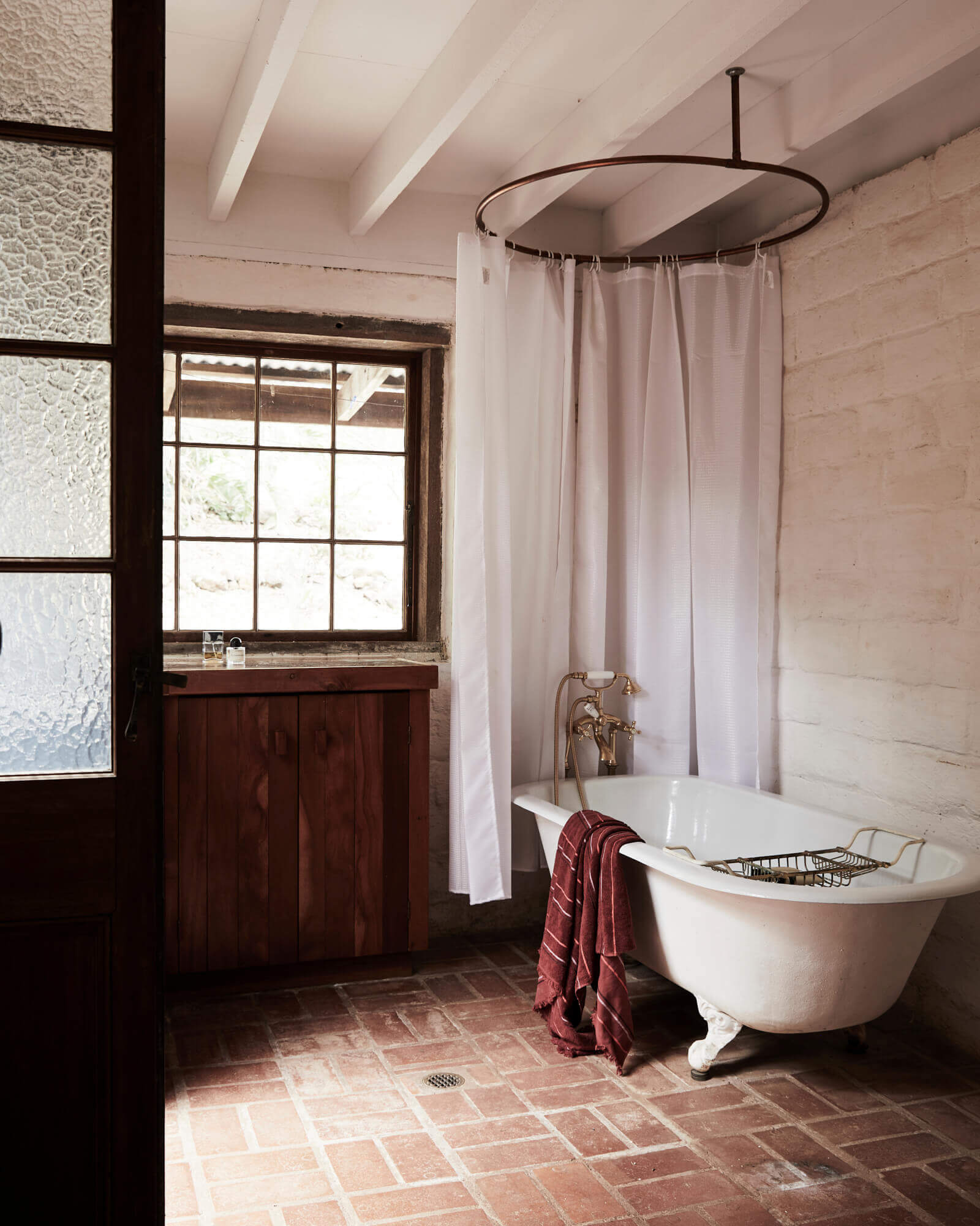Bathroom at The Perch, Byron Beach Abodes with original claw-foot bath, timber doors and windows with mottled glass and round shower curtain rail