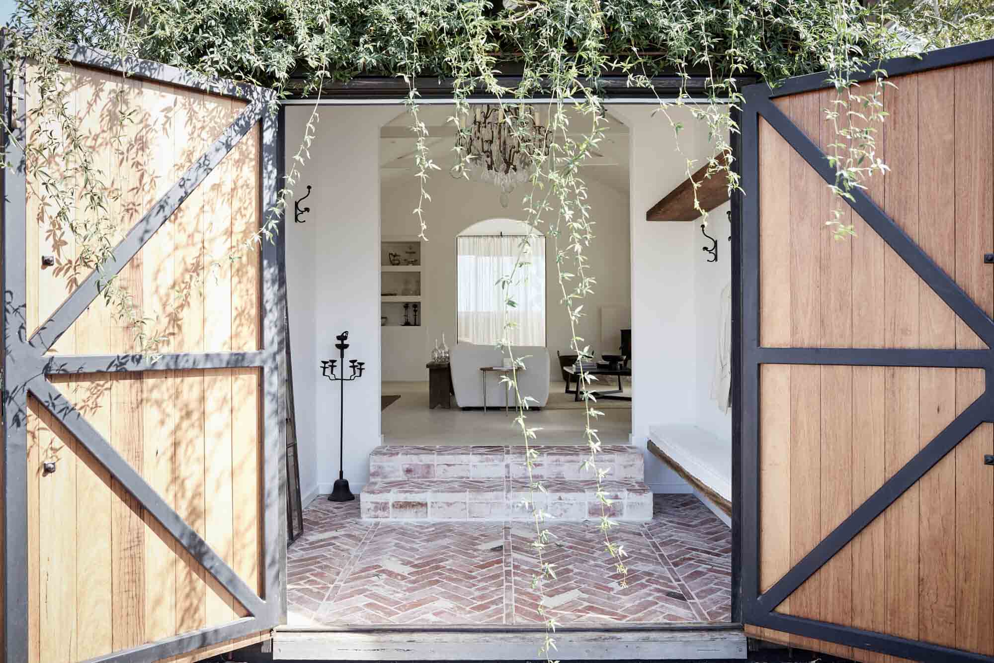 The front entrance to the Le Viti Barn accommodation in Newrybar with hanging vines, rustic barn doors, herringbone brick entry tiles and vintage chandelier
