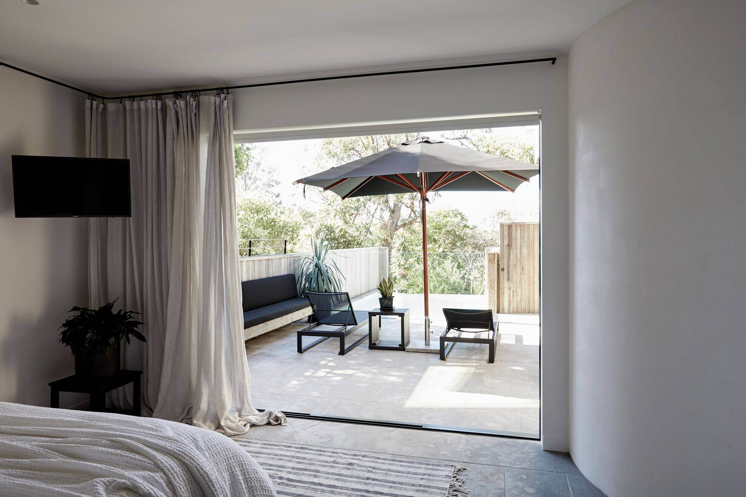 Master bedroom at The Cabin, Byron Beach Abodes overlooking the pool, luxury black daybeds and pool umbrella