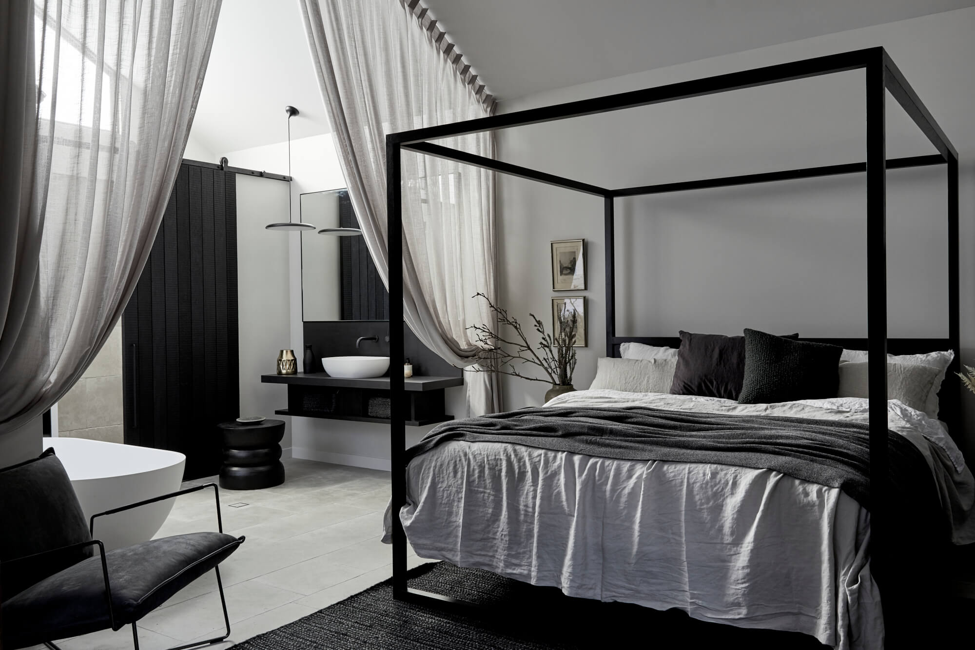 Interior of the Bower Studios, The Bower Byron Bay hotel with black timber four-poster bed, floor to ceiling curtains, luxury linens and open ensuite