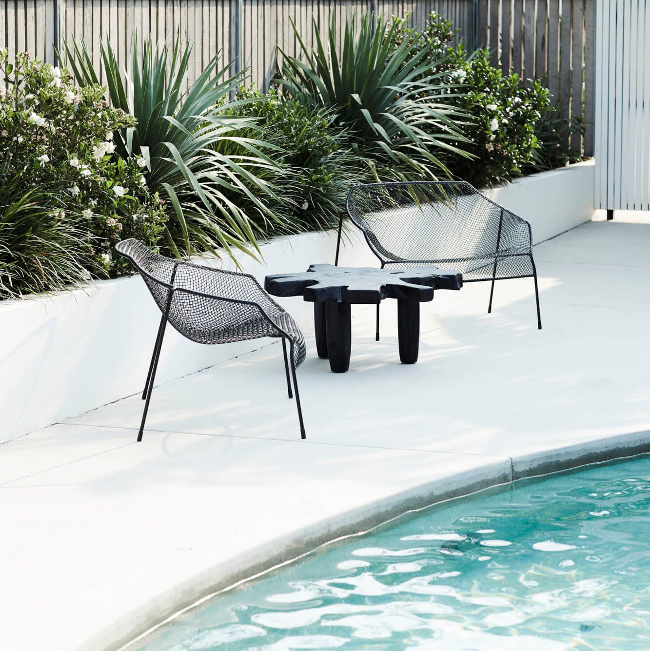 Black metal chairs and timber table sitting poolside at The Bower Byron Bay