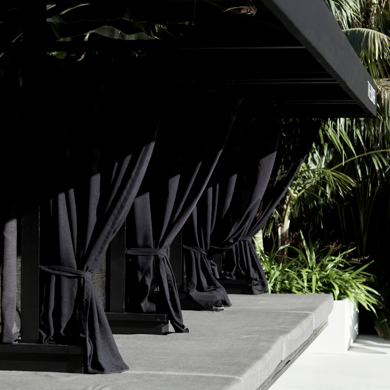 Poolside daybed at The Bower Byron Bay hotel with black roof, black dividing curtains and grey upholstery